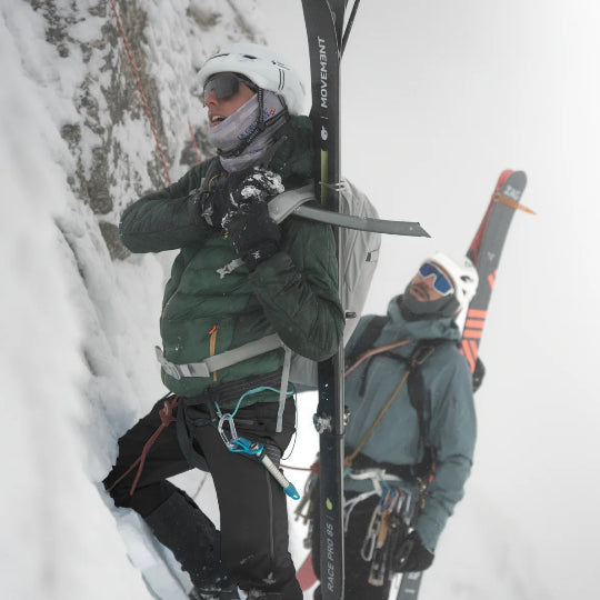Two people with skis and climbing gear in a snowy landscape