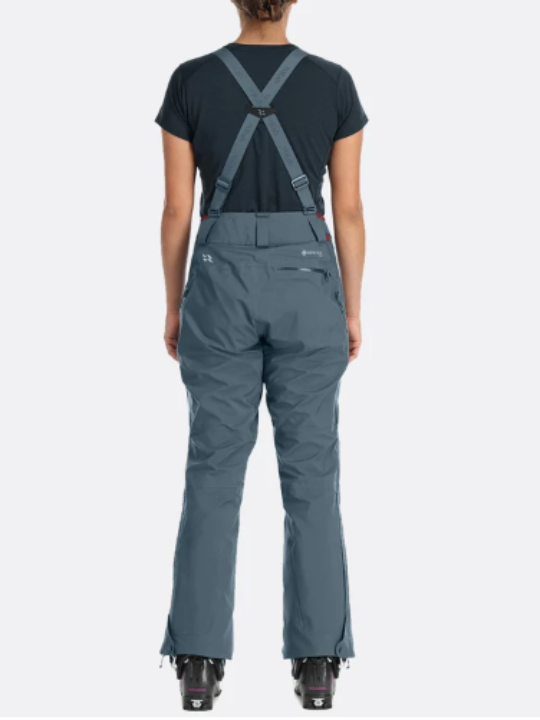A woman wearing gray ski pants with suspenders, designed for ski mountaineering.