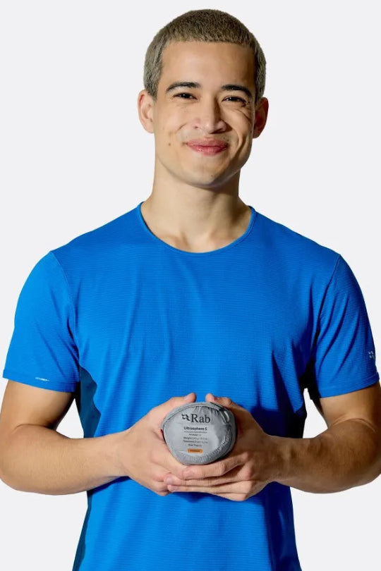 Man wearing a blue shirt holding a packed away sleeping mat against a white background