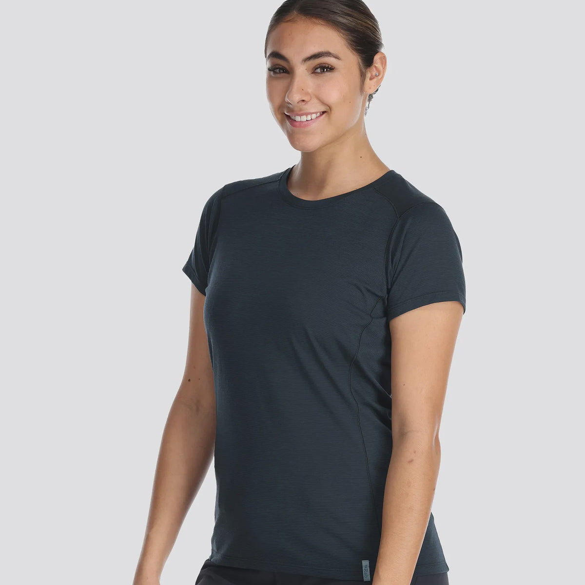 A woman wearing a dark-colored, short-sleeved t-shirt and matching pants designed for mountain activities, standing against a white background.