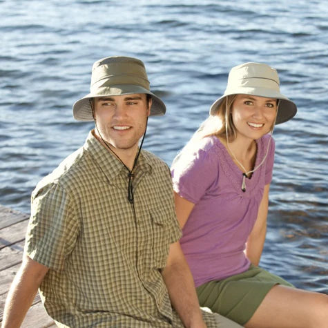 Two people wearing hats sitting by a body of water.