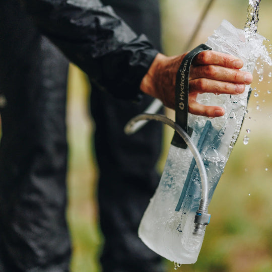 Person filling a water bladder in nature