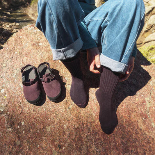 Person wearing purple shoes and socks sitting on a rock with a natural background