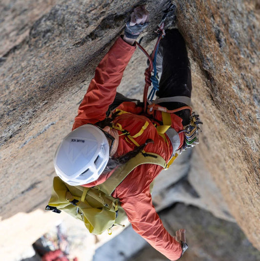 Person climbing a rocky cliff face wearing a helmet and safety gear.