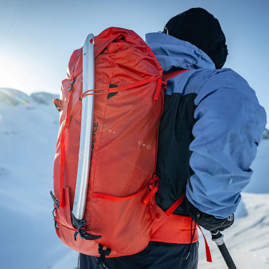 Person with a red backpack and blue jacket standing on a snowy mountain