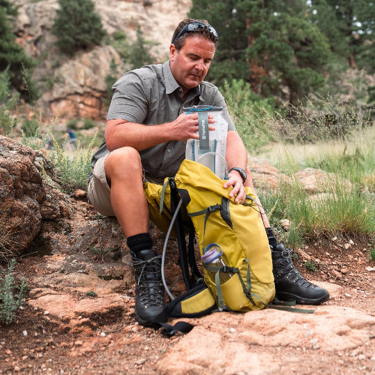 Man sitting outdoors with hiking gear, including a yellow backpack and black boots.