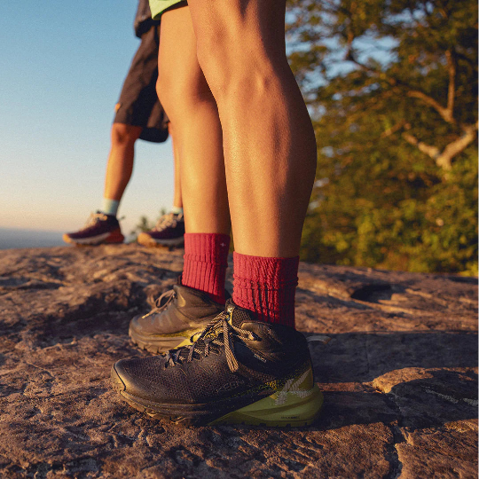 Two people standing on a rocky outcrop with hiking boots and red socks, overlooking a scenic landscape.