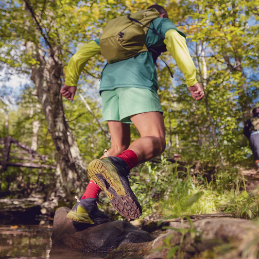 Person hiking through a forest with a backpack, wearing green and yellow outdoor gear.