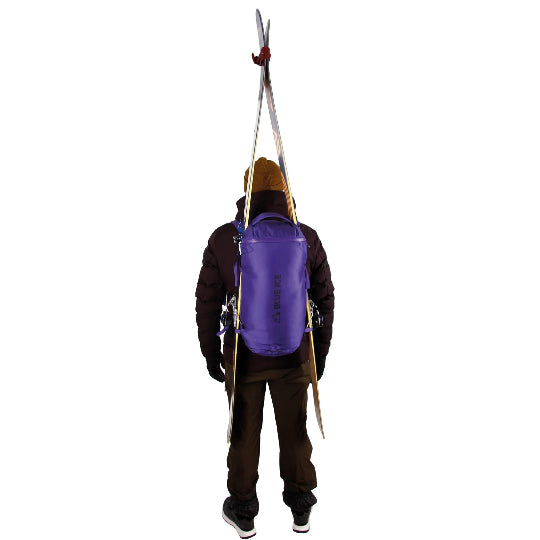 Person wearing a purple backpack with skis attached on a white background