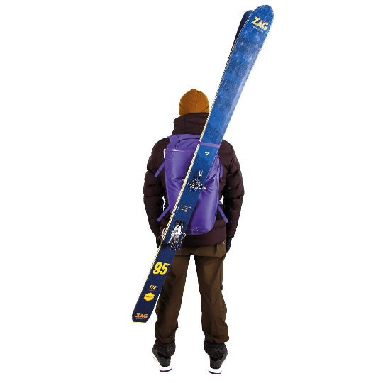 Person carrying a purple backpack with blue skis on a white background