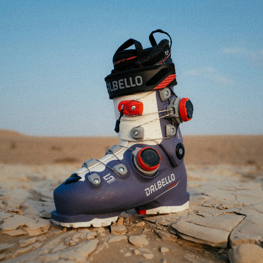 Ski boot with Dalbello branding on a rocky surface with a blue sky.