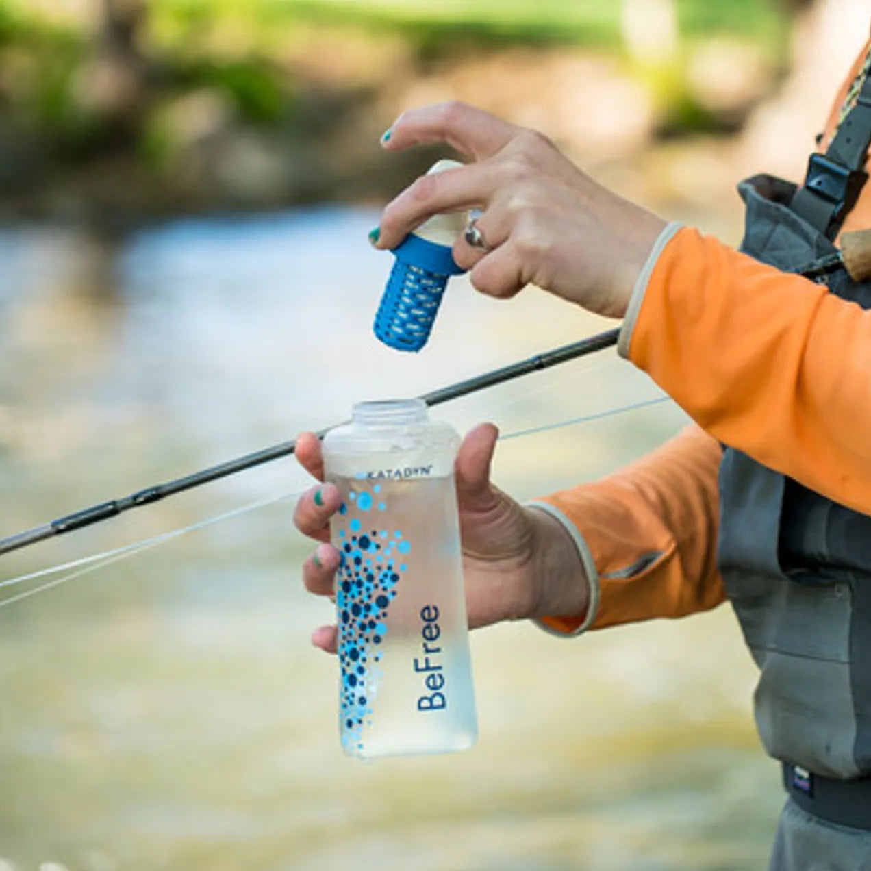 Person holding a water bottle with a filter over a stream