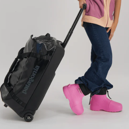 Person wearing pink rain boots with a black suitcase on a light gray background