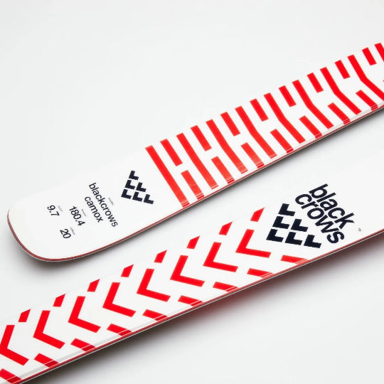Skis with a red and white striped pattern and Black Crows logo in black on a light gray background