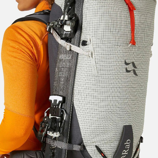 Person wearing a gray backpack with ski equipment on a white background