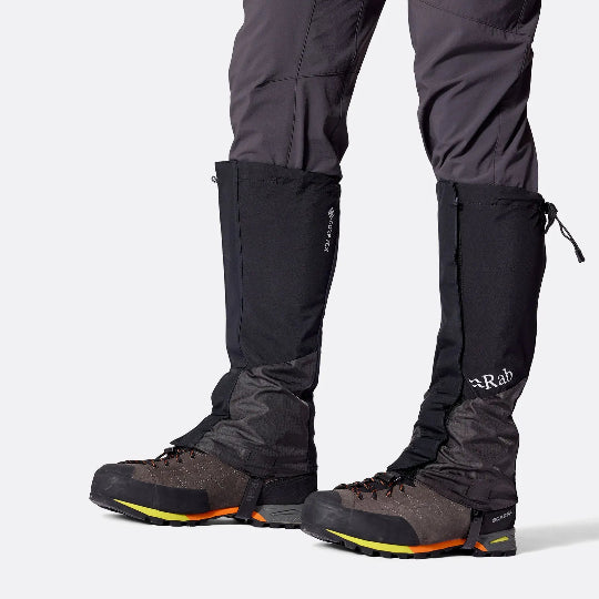 Person wearing black hiking gaiters and shoes on a white background