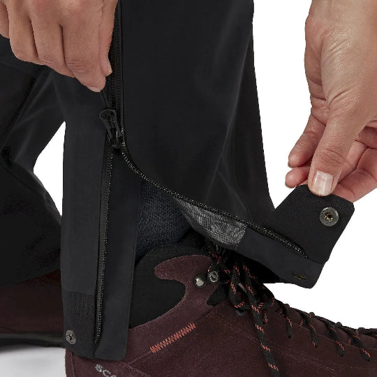 Close-up of a person adjusting a black gaiter on a brown hiking boot with 'Scarpa' branding.