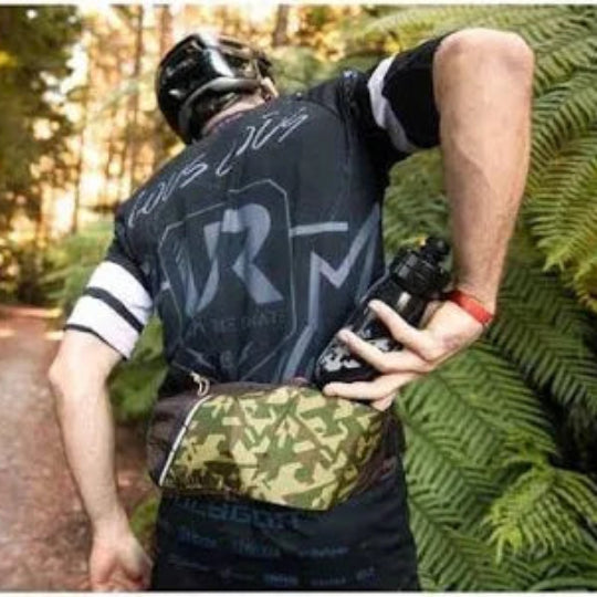 Person in a forest setting wearing a helmet and holding a camera, with 'R' on their shirt.