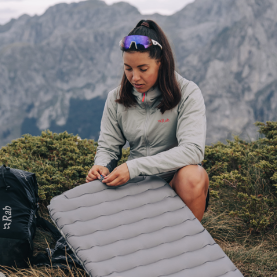 Person setting up a camping mattress in a mountainous area