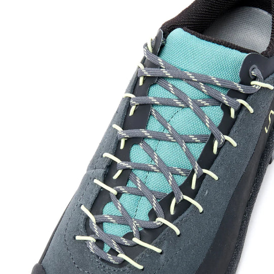 A close-up of a hiking shoe in slate gray suede and black synthetic materials, featuring gray laces with white stitching and a turquoise lining.